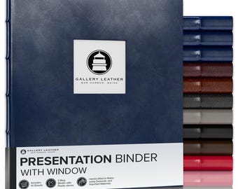 May include: A navy blue presentation binder with a square window on the front cover featuring the Gallery Leather logo. A white label at the bottom reads Presentation Binder with Window. A stack of additional binders in various colors is visible.