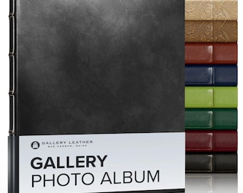 May include: A black photo album with a textured cover and a white band featuring the text Gallery Leather Bar Harbor, Maine Gallery Photo Album. To the right, a vertical stack of eight additional photo albums in tan, brown, blue, green, and black.