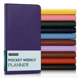 May include: A purple 2027 pocket weekly planner with a textured cover and a light blue paper band featuring the text HARBOR POCKET WEEKLY PLANNER. To the right, a vertical stack of identical planners in yellow, pink, dark green, navy, blue, brown, lilac, rust, orange, and black.