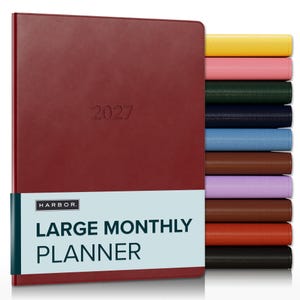 May include: A large 2027 monthly planner with a dark red cover and a light blue paper band featuring the text HARBOR LARGE MONTHLY PLANNER. A stack of additional planners in yellow, pink, green, navy, blue, brown, purple, tan, orange, and black is visible.