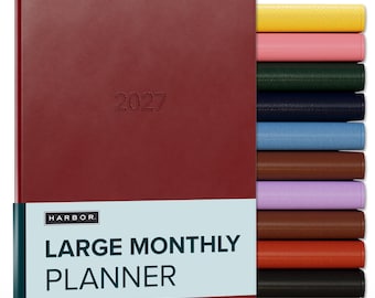 May include: A large 2027 monthly planner with a dark red cover and a light blue paper band featuring the text HARBOR LARGE MONTHLY PLANNER. A stack of additional planners in yellow, pink, green, navy, blue, brown, purple, tan, orange, and black is visible.