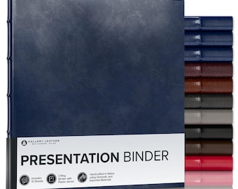 May include: A navy blue presentation binder with a textured finish and a white label featuring the text GALLERY LEATHER BAR HARBOR, MAINE PRESENTATION BINDER. A stack of additional binders in various colors is visible to the right side.