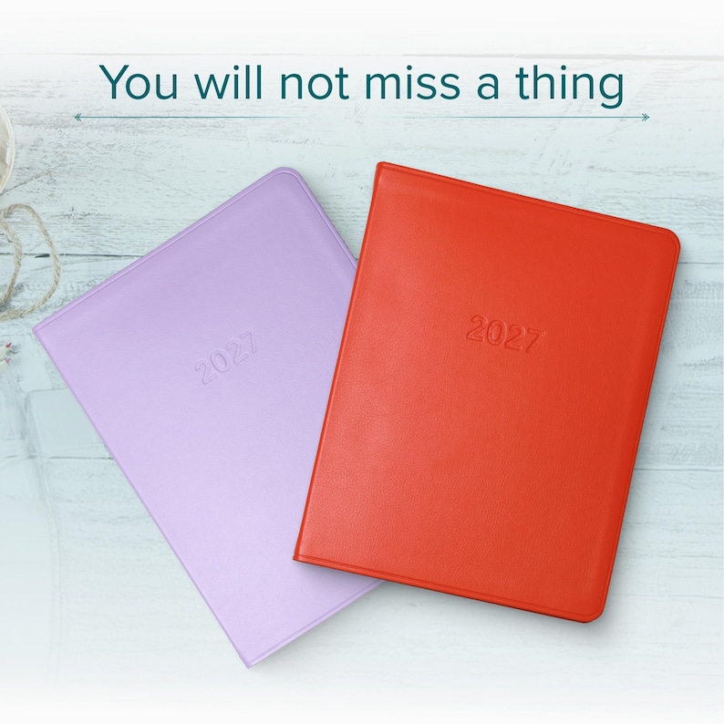 May include: Two rectangular planners, one in light purple and one in bright orange, each embossed with the year 2027 on the front cover. The text "You will not miss a thing" is printed in dark teal above the planners on a light wood background.