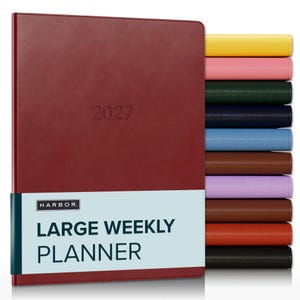 May include: A maroon 2027 large weekly planner with a light blue paper band featuring the text HARBOR LARGE WEEKLY PLANNER. A stack of additional planners in yellow, pink, dark green, navy, light blue, brown, lavender, tan, orange, and black is visible.