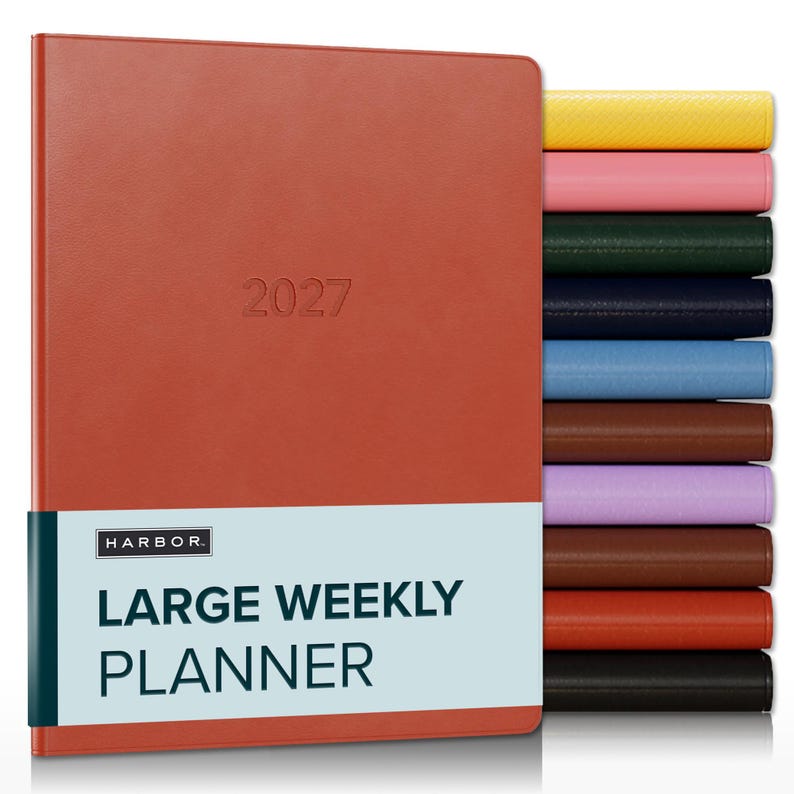 May include: A rust-colored 2027 large weekly planner with a smooth cover, featuring a light blue paper band with the text HARBOR LARGE WEEKLY PLANNER. A stack of additional planners in yellow, pink, green, navy, blue, brown, purple, and black is visible.
