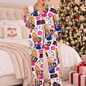 May include: A white long-sleeve button-down pajama set featuring a repeating print of the movie title White Chicks, FBI badges, handcuffs, and pink lips. The pajamas have a notched collar and brown piping along the edges of the shirt and pants.
