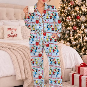 May include: A light blue button-down pajama set featuring a repeating pattern of Peanuts characters, including Snoopy and Charlie Brown, with colorful Christmas lights, snowflakes, and the red text Merry Christmas printed throughout the fabric.