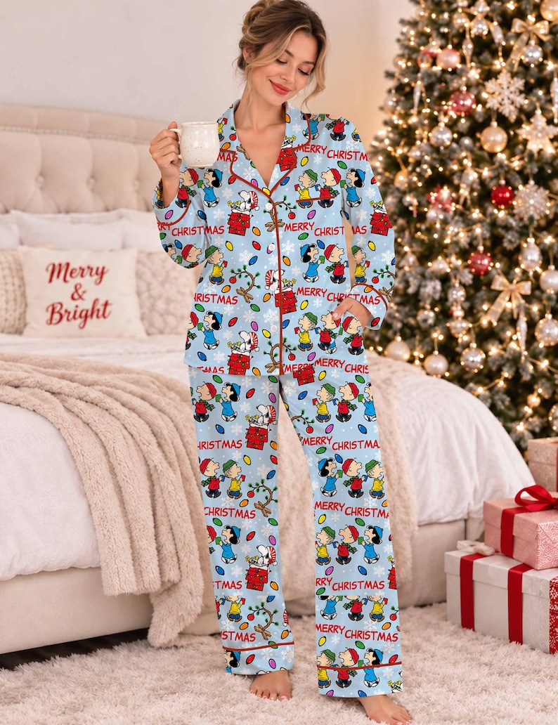 May include: A light blue button-down pajama set featuring a repeating pattern of Peanuts characters, including Snoopy and Charlie Brown, with colorful Christmas lights, snowflakes, and the red text Merry Christmas printed throughout the fabric.