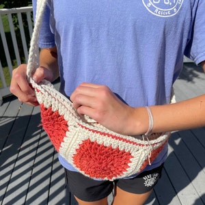 May include: A white and coral crocheted bag with a long strap. The bag is being held open by a person wearing a light blue shirt with a logo that says "Rescue".