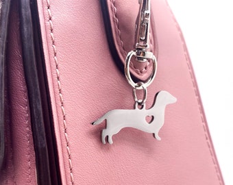 May include: A silver dachshund charm with a heart cutout hangs from a pink handbag.