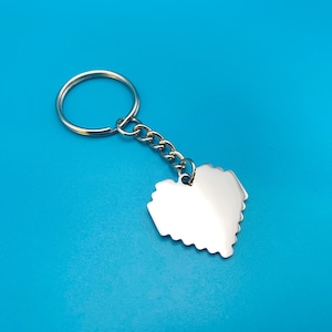May include: A silver key chain with a heart-shaped charm. The heart is made of small squares, giving it a pixelated look.