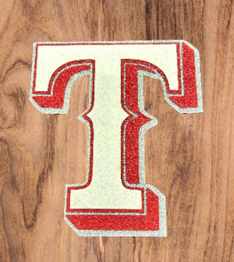 May include: A white letter T with a red outline and glitter. The letter is on a wood background.