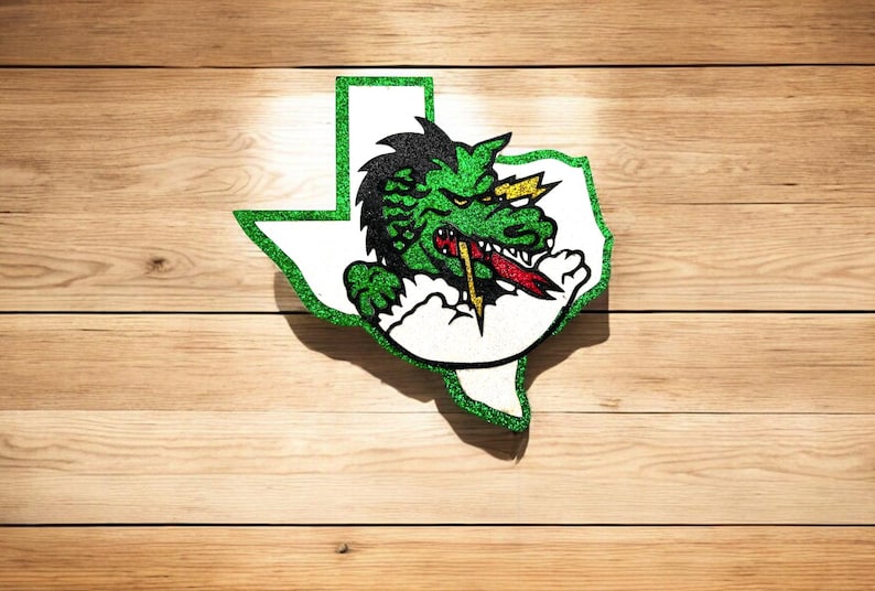 May include: Green glitter outline of the state of Texas with a green, yellow, and red cartoon dragon inside. The dragon is breathing fire and has a menacing expression.