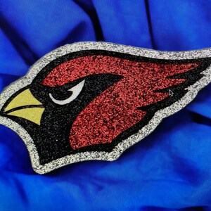 May include: A red, black, and yellow glitter cardinal bird applique. The cardinal is facing left and has a white outline.