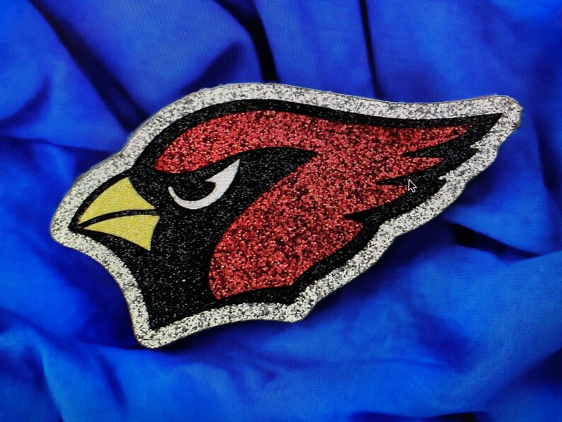May include: A red, black, and yellow glitter cardinal bird applique. The cardinal is facing left and has a white outline.