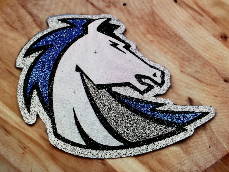 May include: A silver and blue glitter iron-on patch featuring a white horse head with a blue mane. The horse is facing the right side of the image.