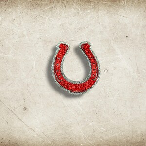 May include: A red glitter horseshoe with a silver glitter border. The horseshoe is a symbol of good luck and is set against a textured, off-white background.