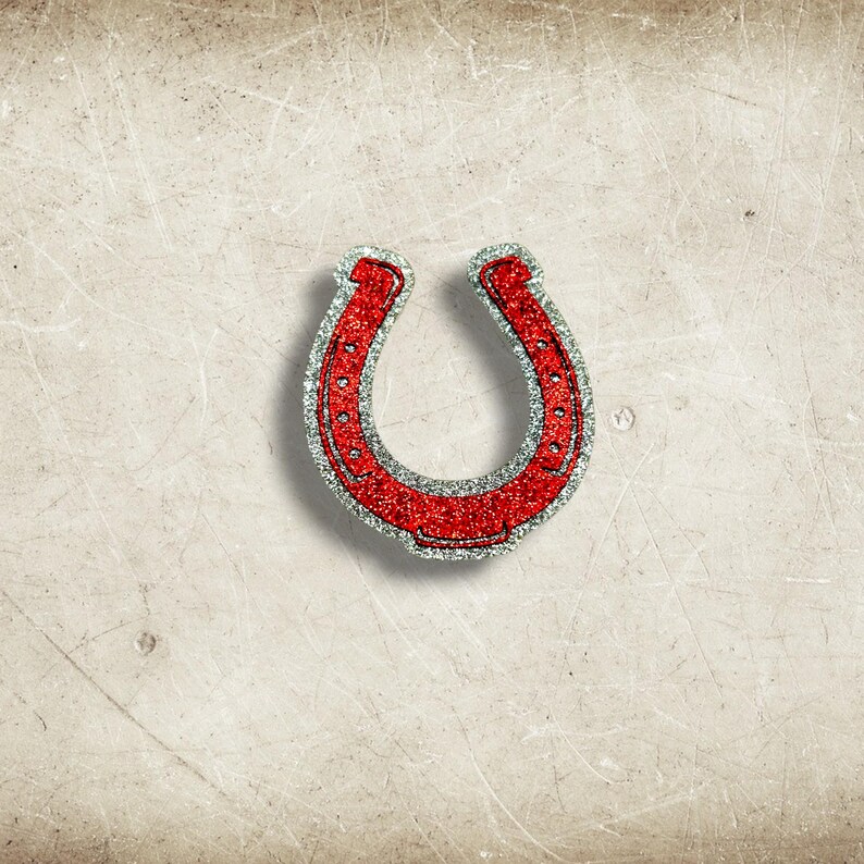 May include: A red glitter horseshoe with a silver glitter border. The horseshoe is a symbol of good luck and is set against a textured, off-white background.