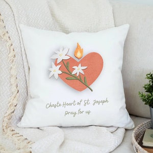 May include: White throw pillow with a red heart and white flowers. The heart has a flame on top and the text "Chapte Heart of St. Joseph Pray for us" is printed below the heart.