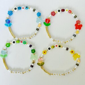 May include: Four beaded bracelets featuring colorful flower, butterfly, and heart-shaped charms, interspersed with white letter beads spelling SHUT UP, HOLD ME, LOVE ME, and WATCH THIS, accented with gold-toned twisted metal tubes and small beads.