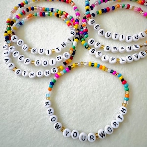 May include: Colorful beaded bracelets with white letter beads spelling out inspirational phrases like "You Got This," "Be Brave," and "Know Your Worth." The bracelets feature a mix of vibrant colors and gold accents.