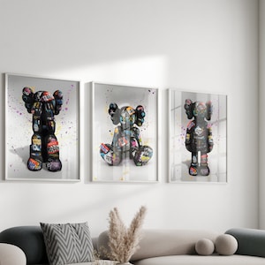 May include: Three framed prints of colourful, graffiti-style art featuring a cartoon character. The character is black and white with colourful accents and is depicted in three different poses.