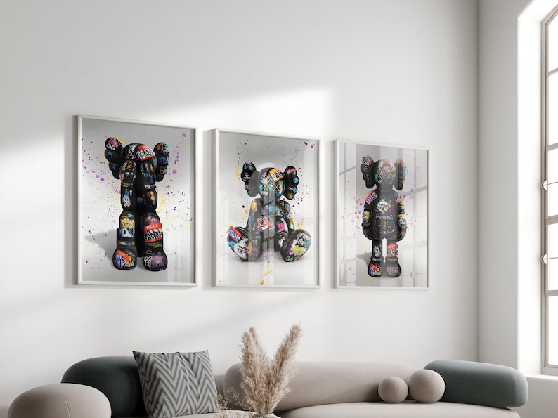 May include: Three framed prints of colourful, graffiti-style art featuring a cartoon character. The character is black and white with colourful accents and is depicted in three different poses.