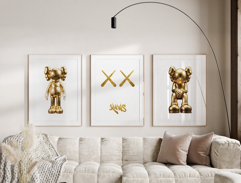 May include: Three framed prints featuring gold-coloured illustrations of a cartoon character. The centre print displays a pair of crossed-out Xs with the word "AWWS" written beneath.