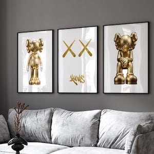 May include: Three framed prints with a white background. The centre print features a gold 'XX' design. The prints on the left and right feature a gold figurine of a character with a blank expression. The figurine on the left is standing and the figurine on the right is sitting.