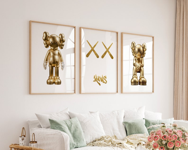 May include: Three framed prints featuring gold-coloured sculptures of a cartoon character. The character is depicted in three different poses: standing, with crossed arms, and sitting. The prints are hung on a white wall above a sofa.