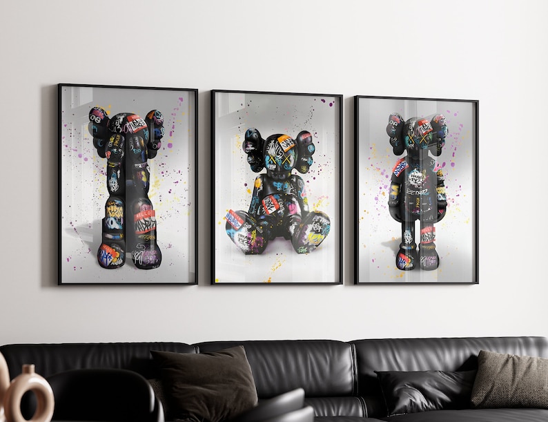 May include: Three framed prints of black and white figures with colourful graffiti-style designs. The figures are standing, sitting, and standing with their arms raised.
