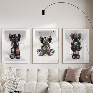 May include: Three framed prints of black and white figures with colourful details. The figures are in different poses, one standing, one sitting, and one with arms crossed. The background is white with colourful paint splatters.