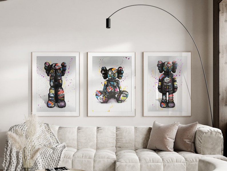 May include: Three framed prints of black and white figures with colourful details. The figures are in different poses, one standing, one sitting, and one with arms crossed. The background is white with colourful paint splatters.
