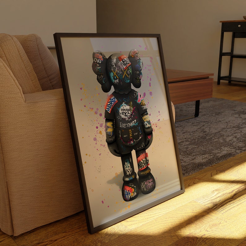 May include: A framed print of a black and white graffiti-style illustration of a cartoon character. The character is standing on a beige background with colourful paint splatters.
