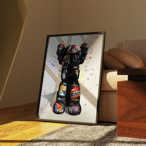 May include: A black and white illustration of a graffiti-covered toy figure with colourful paint splatters on a white background. The figure has a large head with a small body and is wearing a red "HELLO" sticker on its leg.