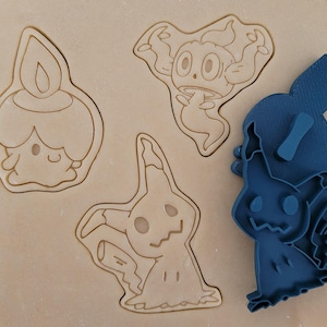 Può includere: Tre stampini per biscotti, uno blu, uno bianco e uno marrone, a forma di personaggi Pokémon. Lo stampino blu è un Gengar, lo stampino bianco è un Gastly e lo stampino marrone è un Litwick.