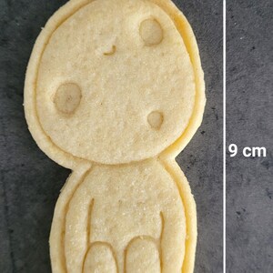 May include: A Kodama-shaped cookie, approximately 3.5 inches tall and 2 inches wide, with three circular indentations and a smiling face. The cookie is light brown and has a textured surface. The word "Kodama" is printed at the bottom.