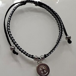 May include: A black and silver braided bracelet with a silver button charm.