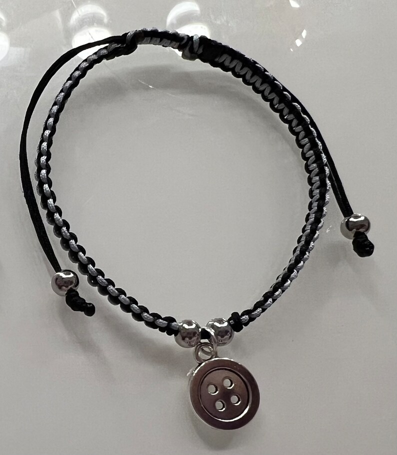 May include: A black and silver braided bracelet with a silver button charm.