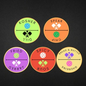 Puede incluir: Seis etiquetas redondas de colores con diferentes sabores y nombres de pepinillos. Las etiquetas tienen un diseño de pepinillo y pala. Los sabores son: Kosher Dill, Fried Jarred, Sour Spicy, Chip Spear, Bread & Butter y Gherkins.
