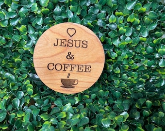May include: A round wooden coaster with the text "JESUS & COFFEE" and a heart symbol above the word "JESUS". A small coffee cup with steam coming from it is below the text.