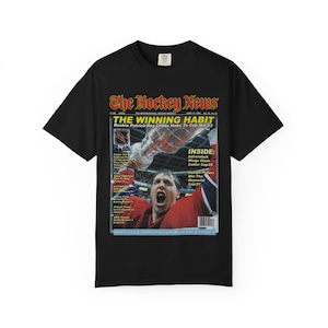 May include: Black t-shirt with a vintage "The Hockey News" magazine cover design. The cover depicts a hockey player celebrating with a trophy, and the headline reads "THE WINNING HABIT." Text includes "Rookie Patrick Roy Leads Habs To Cup No. 23."