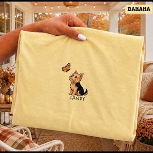 Folded BANANA Comfort Colors shirt with cute Yorkshire Terrier puppy and butterfly graphic, personalized dog lover tee with custom pet name, minimalist pet shirt flat lay aesthetic gift idea.