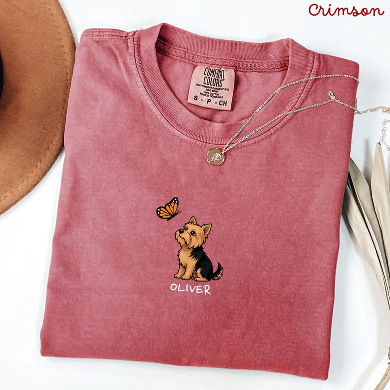 Folded CRIMSON Comfort Colors shirt with cute Yorkshire Terrier puppy and butterfly graphic, personalized dog lover tee with custom pet name, minimalist pet shirt flat lay aesthetic gift idea.