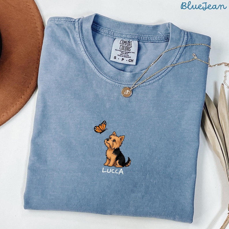 Folded BLUE JEAN Comfort Colors shirt with cute Yorkshire Terrier puppy and butterfly graphic, personalized dog lover tee with custom pet name, minimalist pet shirt flat lay aesthetic gift idea.