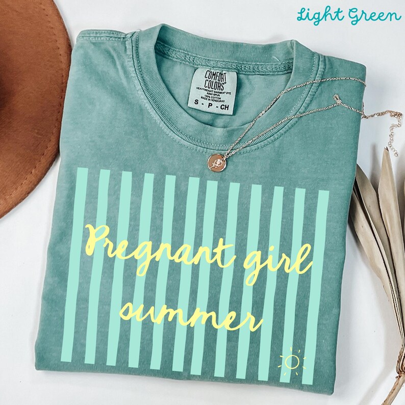 Light green Comfort Colors shirt with vertical mint green stripes and yellow script text reading “Pregnant girl summer” centered across the front, with a small yellow sun icon detail at the bottom corner.