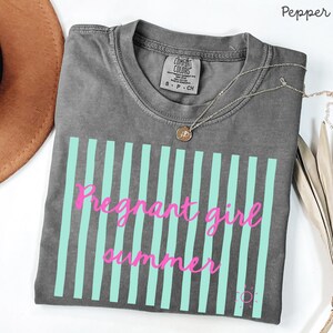 Pepper Comfort Colors shirt with vertical mint green stripes and pink script text reading “Pregnant girl summer” centered across the front, with a small pink sun icon detail at the bottom corner.