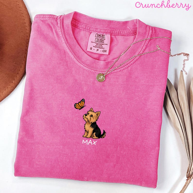 Folded CRUNCHBERRY Comfort Colors shirt with cute Yorkshire Terrier puppy and butterfly graphic, personalized dog lover tee with custom pet name, minimalist pet shirt flat lay aesthetic gift idea.