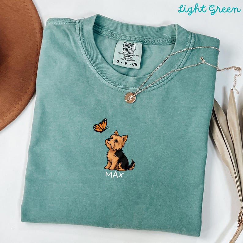 Folded LIGHT GREEN Comfort Colors shirt with cute Yorkshire Terrier puppy and butterfly graphic, personalized dog lover tee with custom pet name, minimalist pet shirt flat lay aesthetic gift idea.