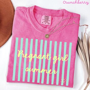 Crunchberry pink Comfort Colors shirt with vertical mint green stripes and yellow script text reading “Pregnant girl summer” centered across the front, with a small yellow sun icon detail at the bottom corner.
